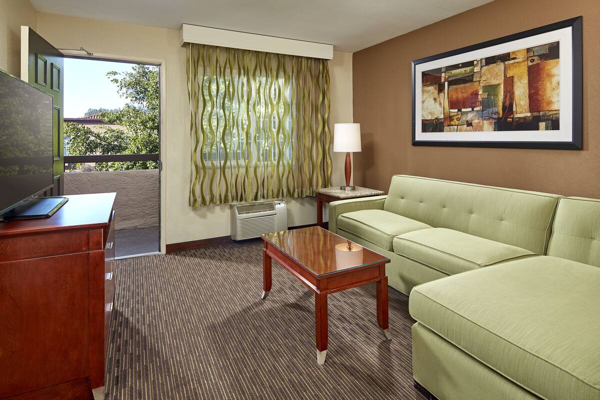 A hotel room with a green sofa, a wooden desk, a lamp, and a painting on the wall.