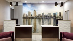 A reception area with two reception desks, a large cityscape mural, and two red upholstered chairs. - Mission View Inn & Suites San Diego Sea World - Zoo (San Diego)