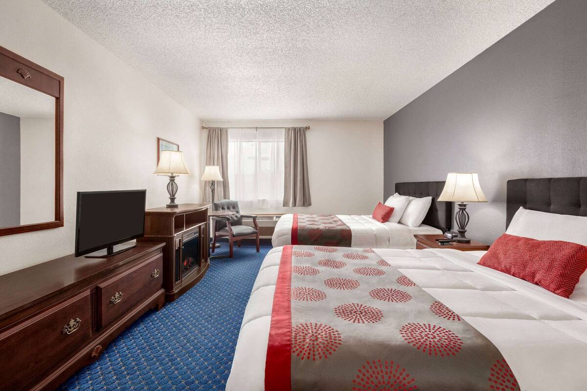 A hotel room with a large bed, a smaller bed, a desk with a TV, a chair, and a window with curtains.