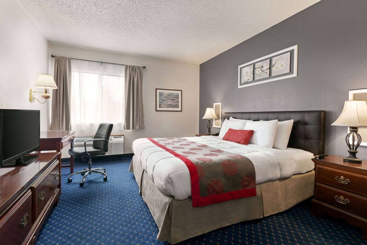 A hotel room with a bed, a desk with a TV, a chair, and a dresser.