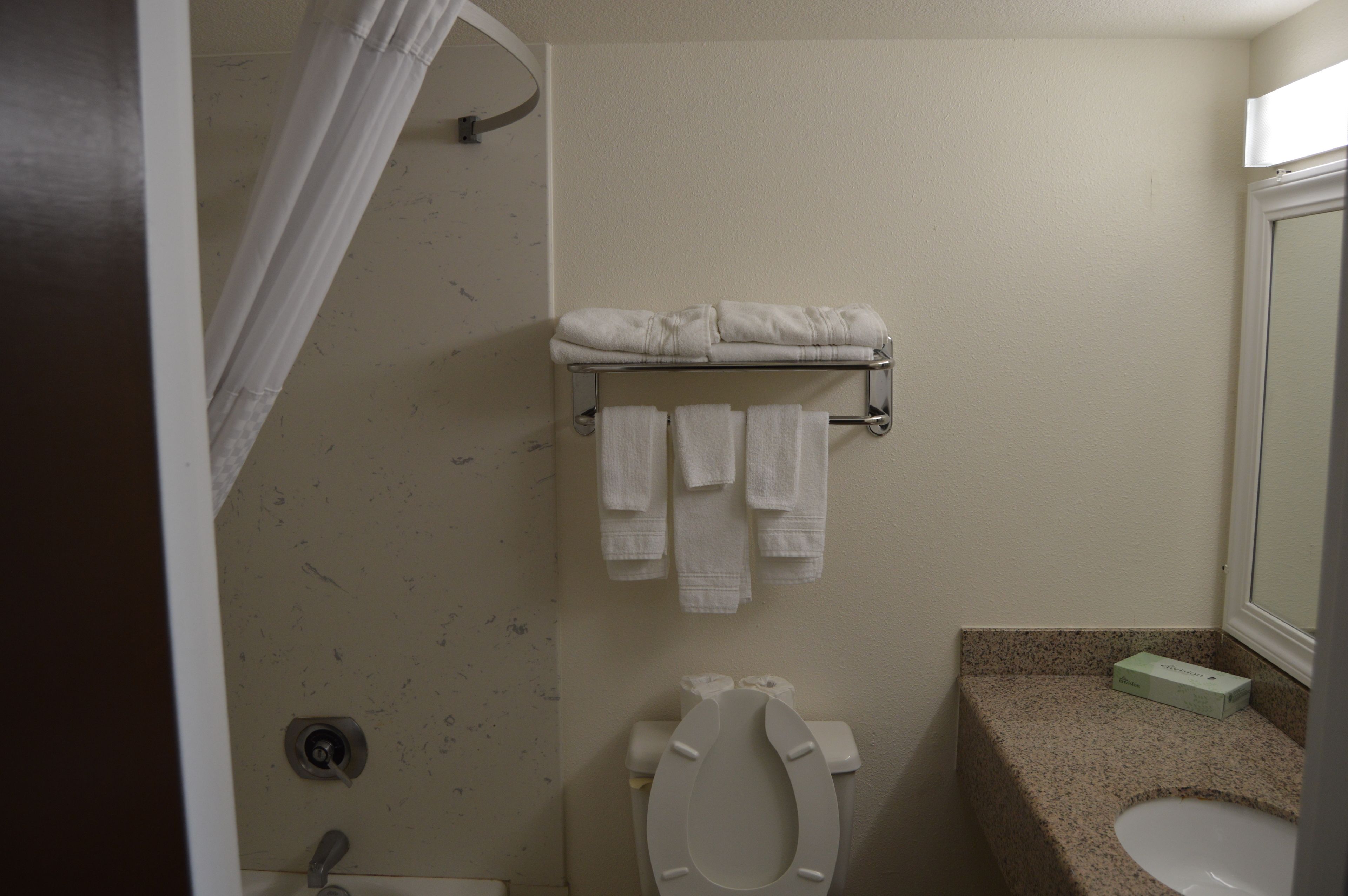 Een badkamer met toilet, wastafel, handdoekrek met handdoeken en een douchegordijn.