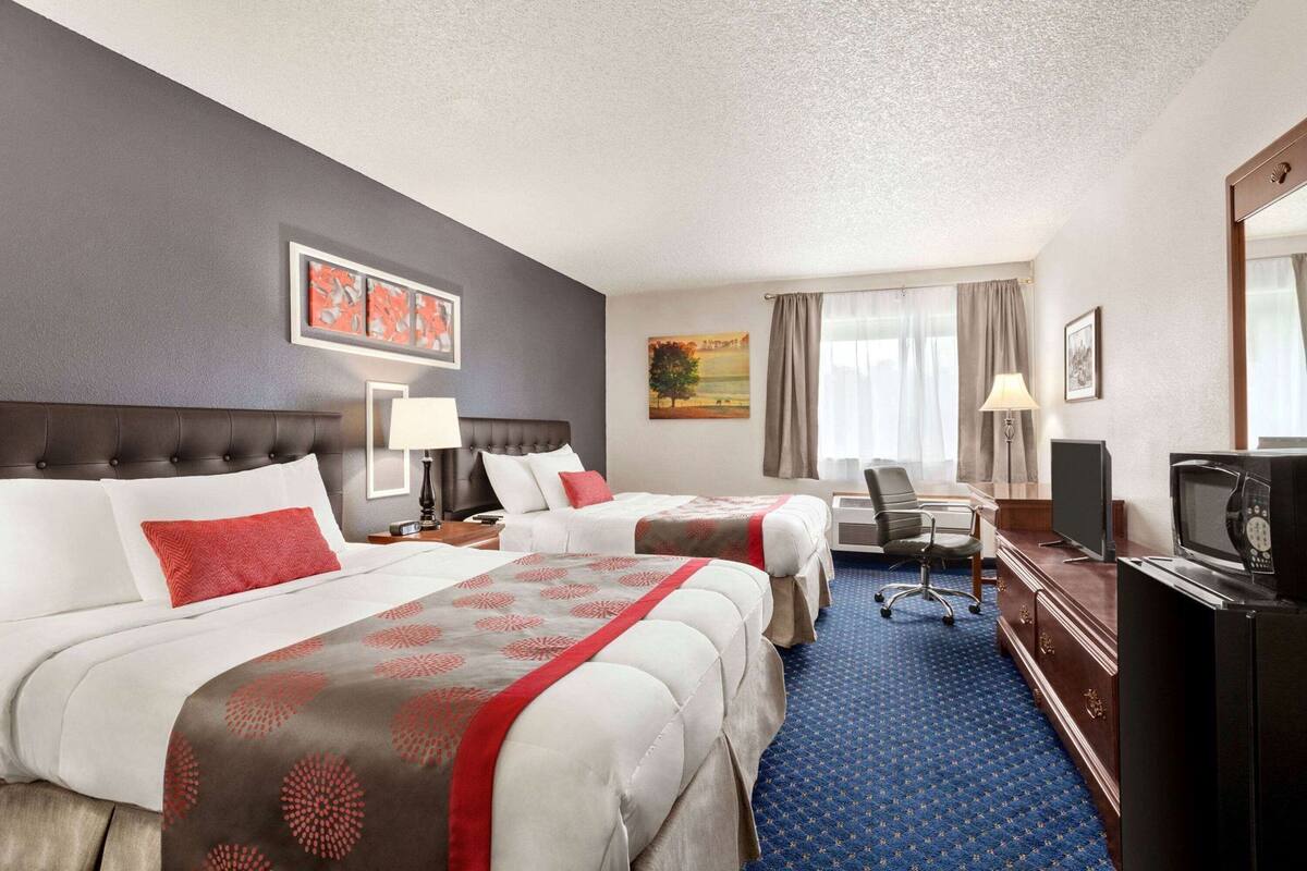 A hotel room with two beds, a desk, a television, and a window with curtains.