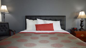 A neatly made bed with a white and red patterned bedspread, a black upholstered headboard, and two bedside tables with lamps.