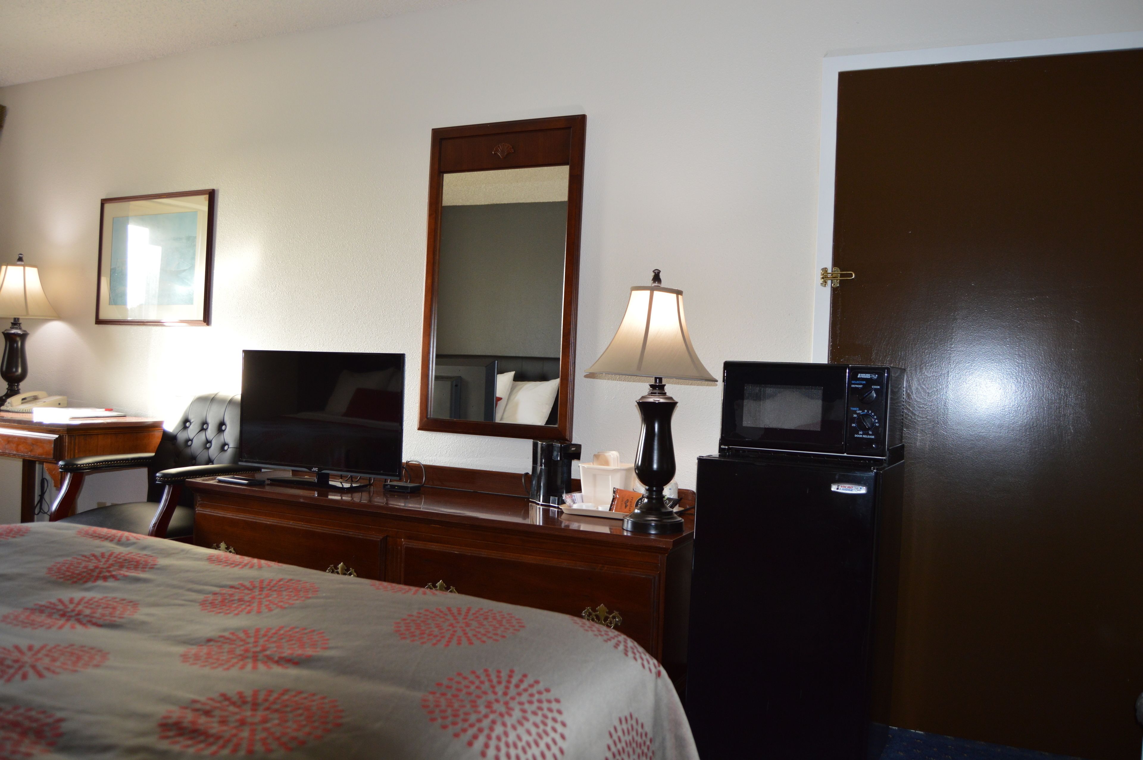 Habitación de hotel con cama, escritorio con computadora, televisor, espejo, refrigerador y puerta.