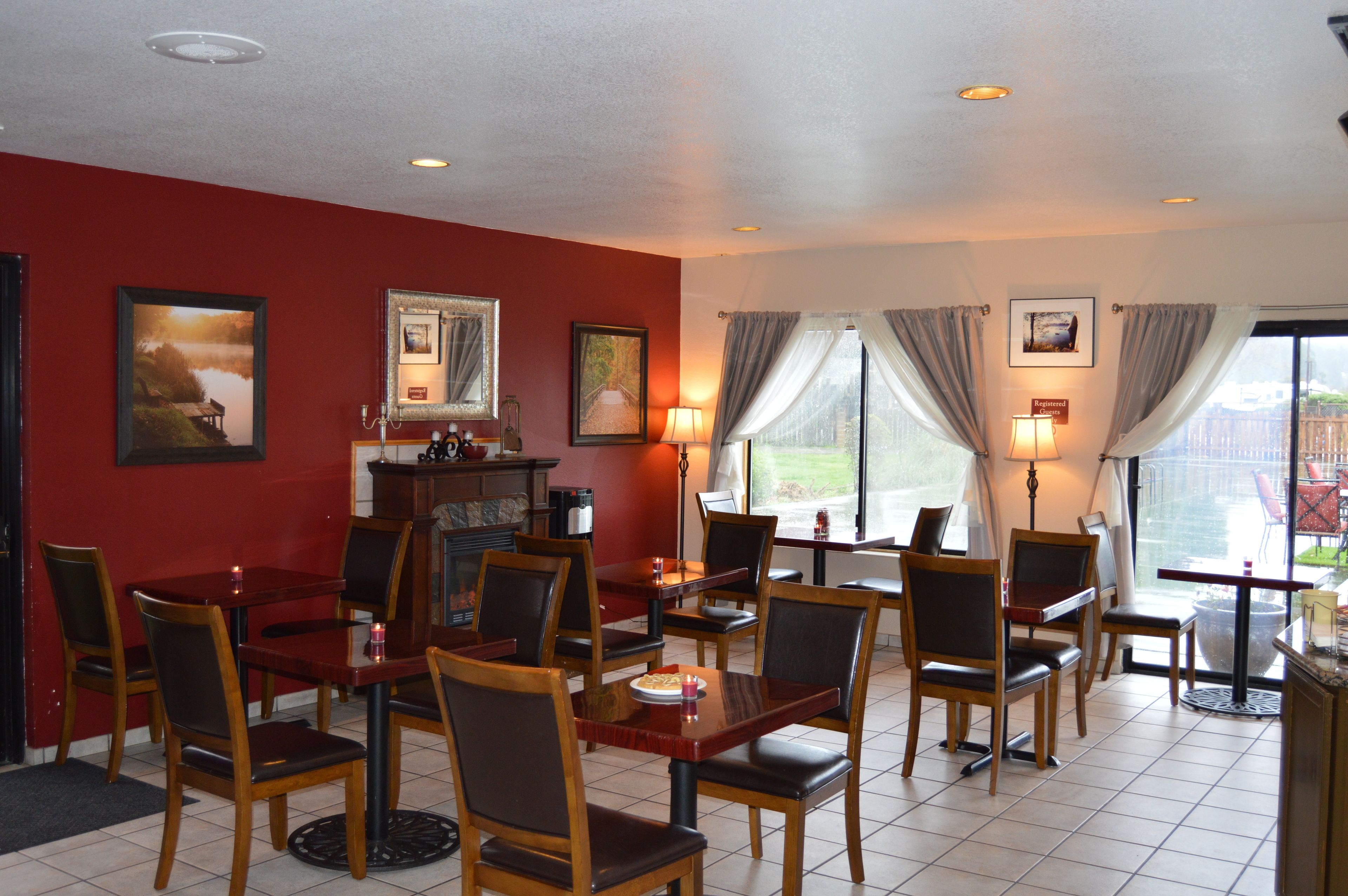 Un restaurant aux murs rouges, avec des tables et des chaises en bois. Les murs sont ornés de tableaux encadrés et il y a une fenêtre avec des rideaux.