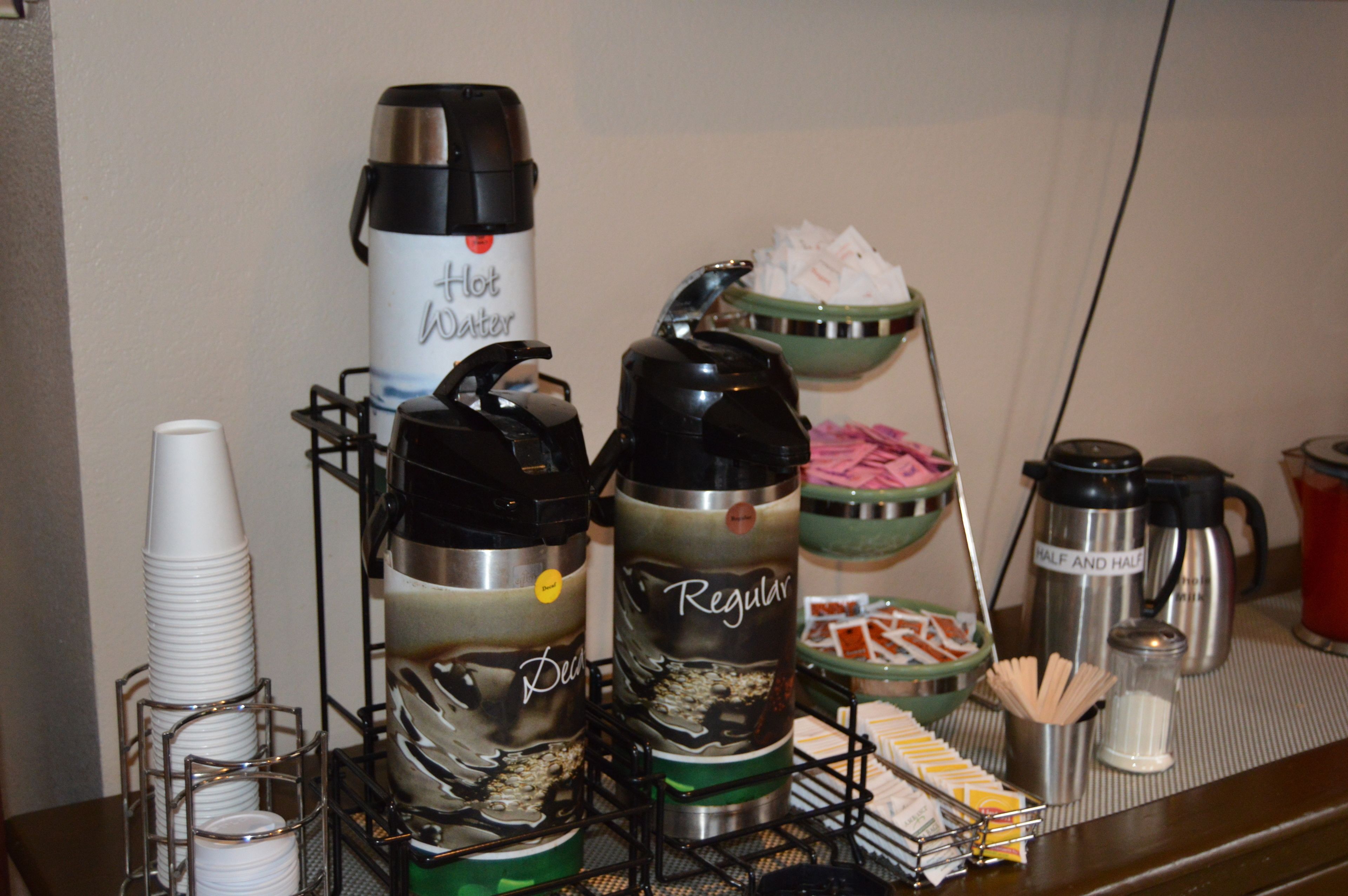 A buffet setup with various hot beverage dispensers, a bowl of napkins, and a coffee maker.