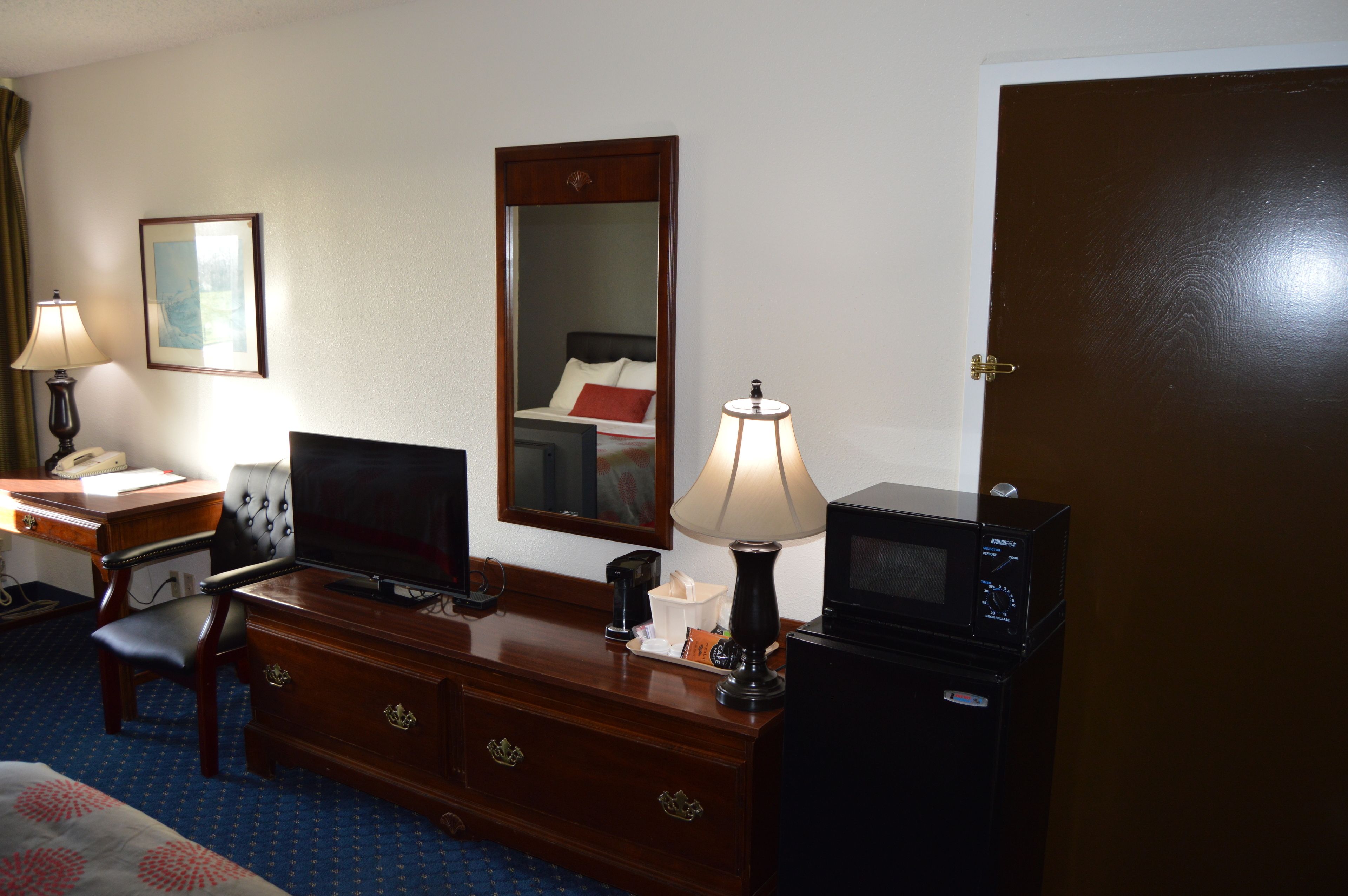 Una habitación de hotel con cama, escritorio con lámpara, televisión, espejo y microondas.