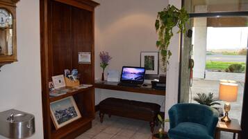 Un área de recepción con un escritorio de madera, una computadora portátil, un cuadro enmarcado, un banco, una planta en maceta y un reloj de pared.