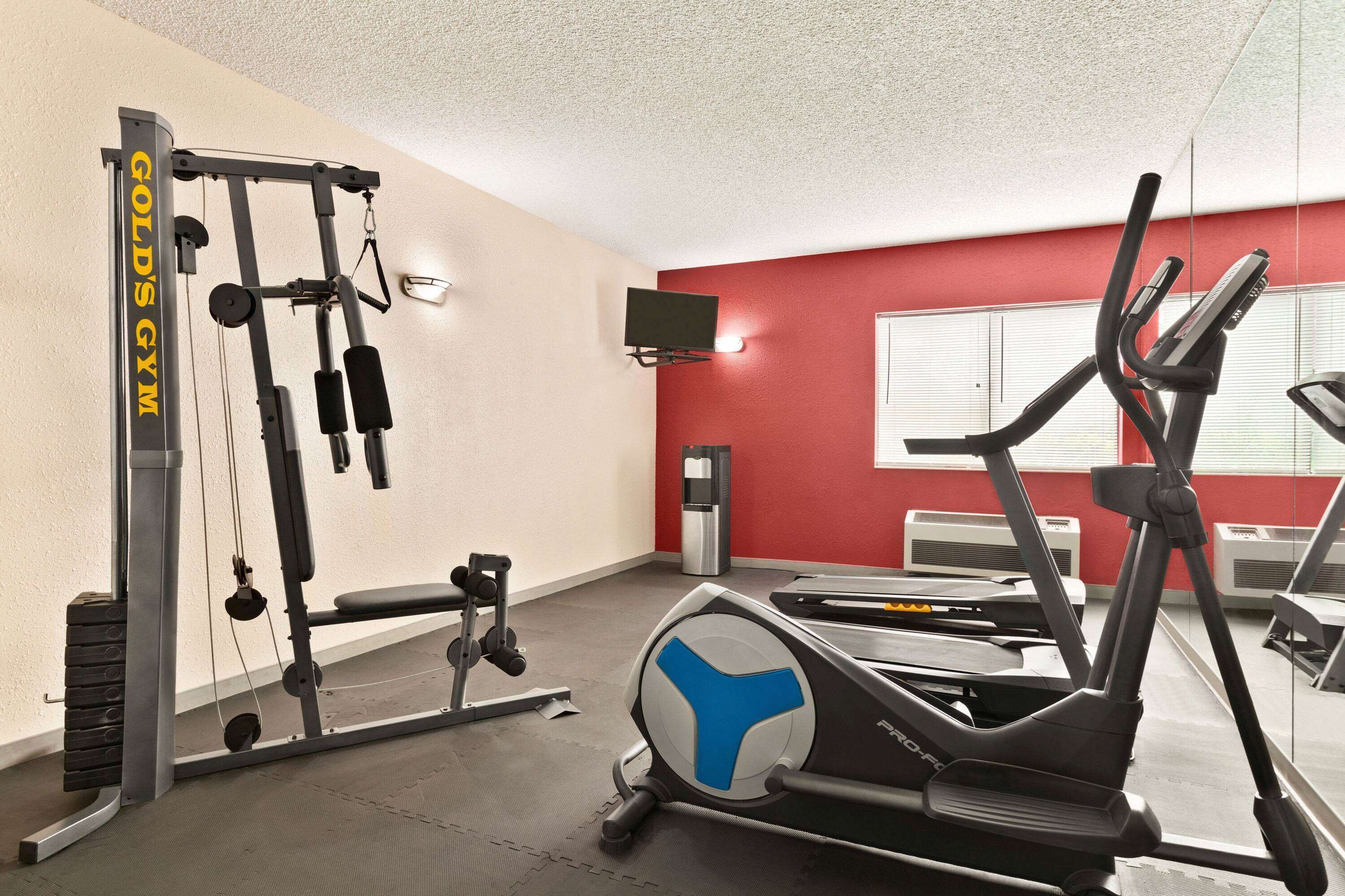 A gym with exercise equipment, a television on the wall, and a window with blinds.