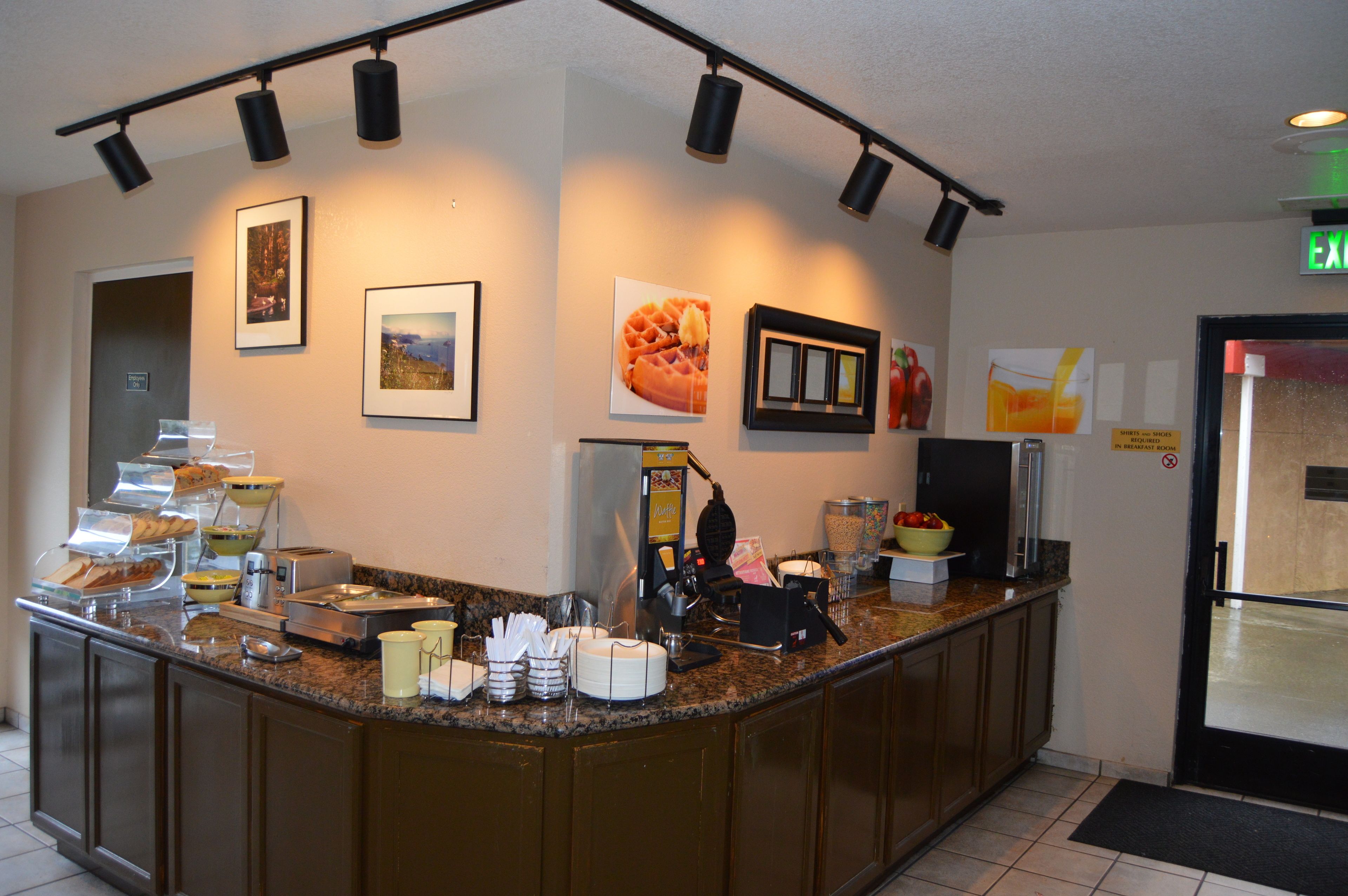 Zona de desayuno de hotel con barra de buffet, que incluye diversas opciones de comida y una máquina de café.