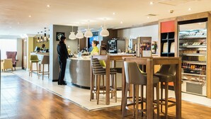 A modern bar area with wooden furniture, pendant lighting, and a display case with baked goods.