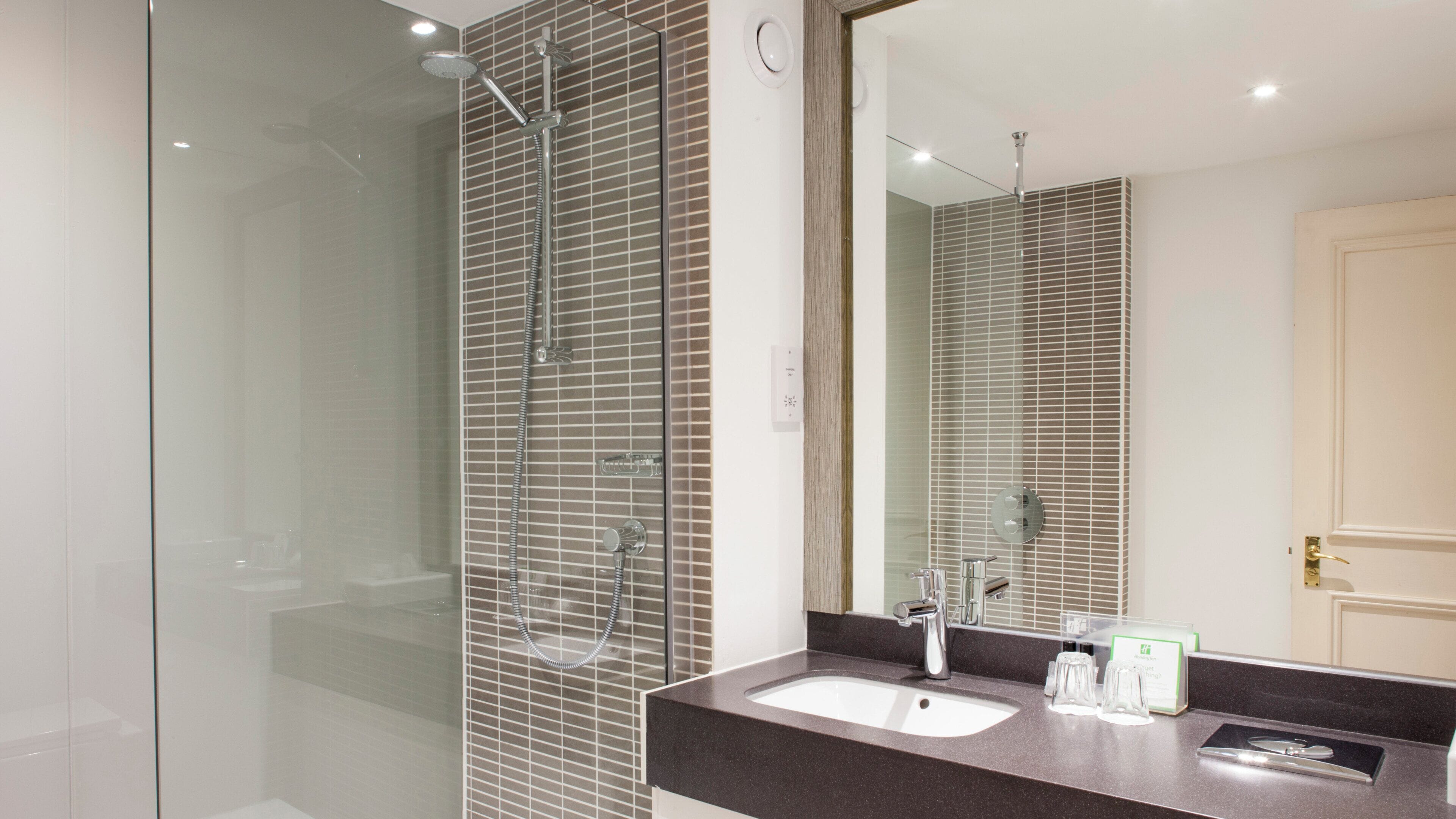Un baño moderno con cabina de ducha de vidrio, un lavabo con encimera oscura y un espejo grande.