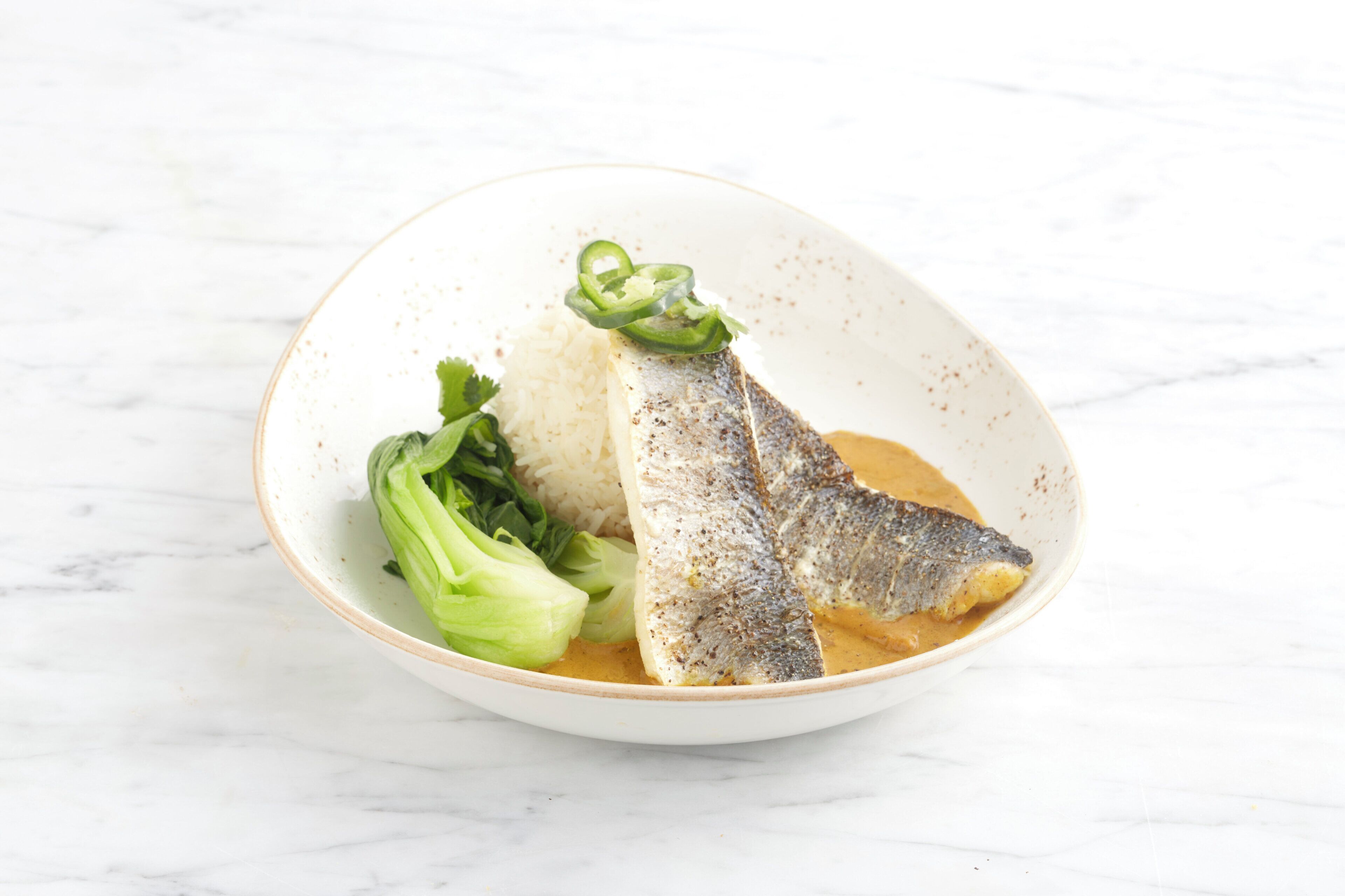 A bowl of fish with rice and vegetables on a white surface.
