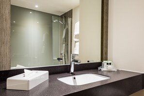 A modern bathroom with a granite countertop, a white sink, a chrome faucet, a glass shower enclosure, and a large mirror.
