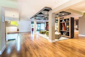A spacious hotel lobby with a wooden floor, a reception desk, and a seating area with tables and chairs.