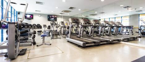 A gym with treadmills, weight machines, and a television screen.