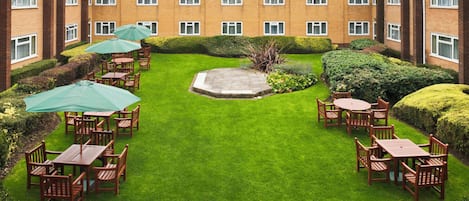 A courtyard with a lawn, seating area, and a building with multiple windows.