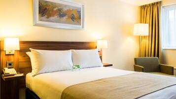 A hotel room with a large bed, two bedside tables with lamps, a chair, a painting on the wall, and a window with curtains.