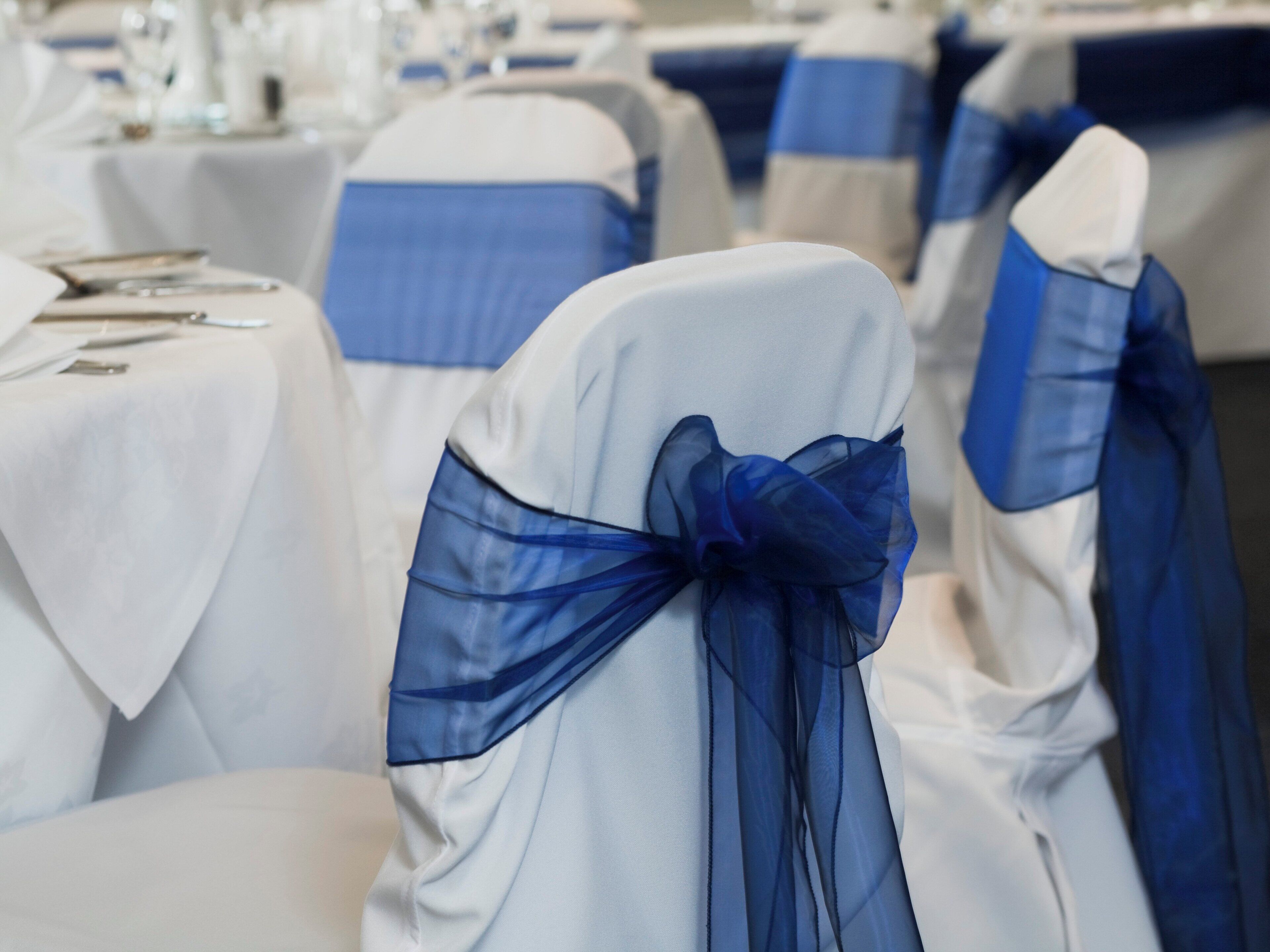 Rows of tables with white tablecloths and blue sashes.