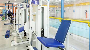 A gym with exercise equipment, a blue chair, and a pool area.