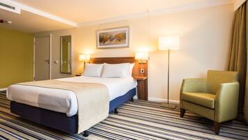 A hotel room with a large bed, two bedside lamps, a chair, and a painting on the wall.