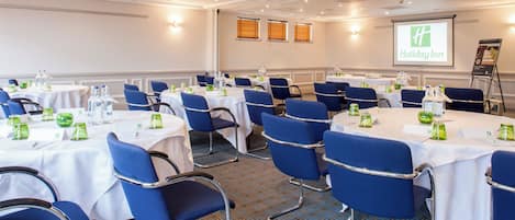 A conference room with round tables, blue chairs, and white tablecloths.