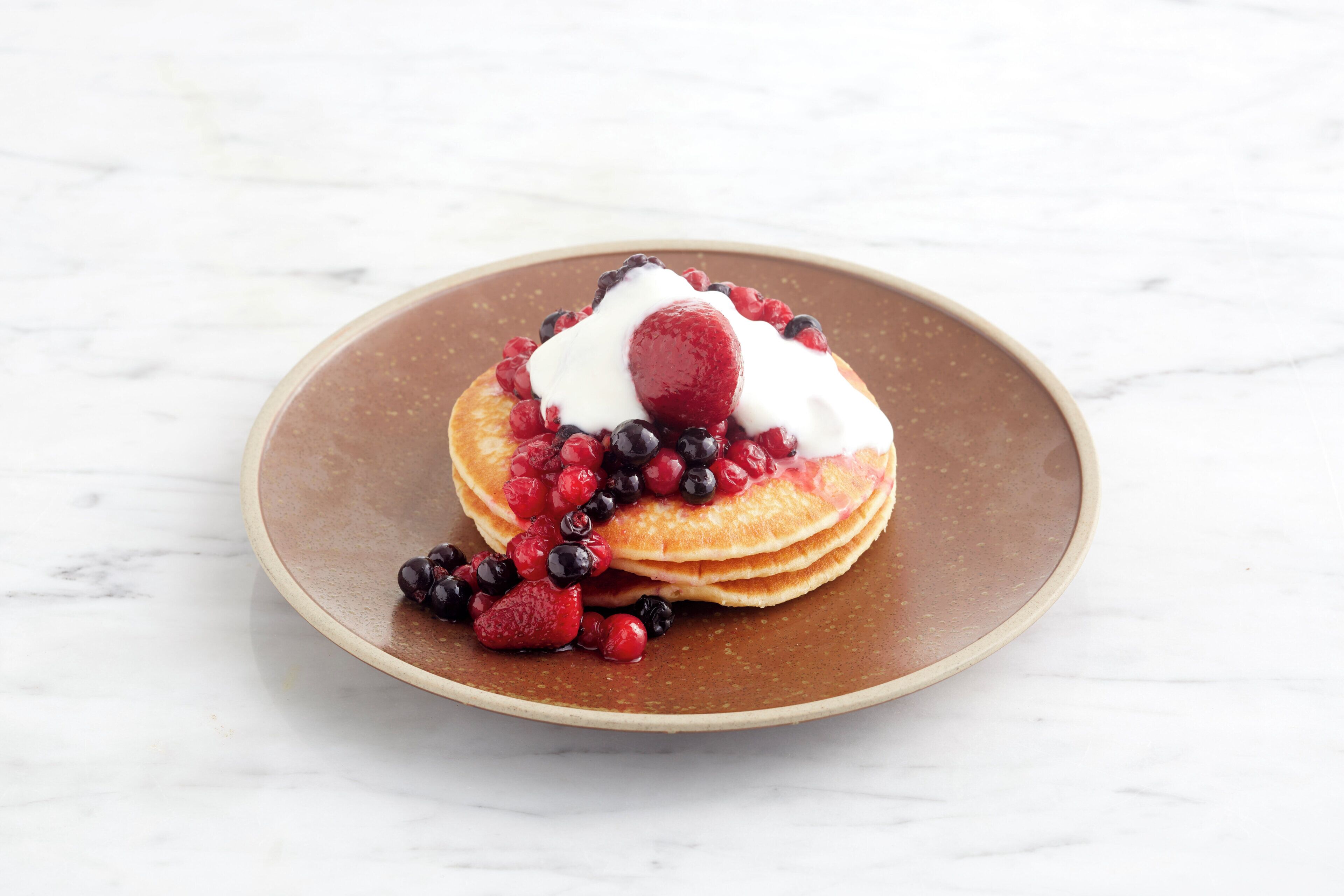 Une pile de crêpes garnie de fruits rouges et de crème fouettée, présentée sur une assiette.