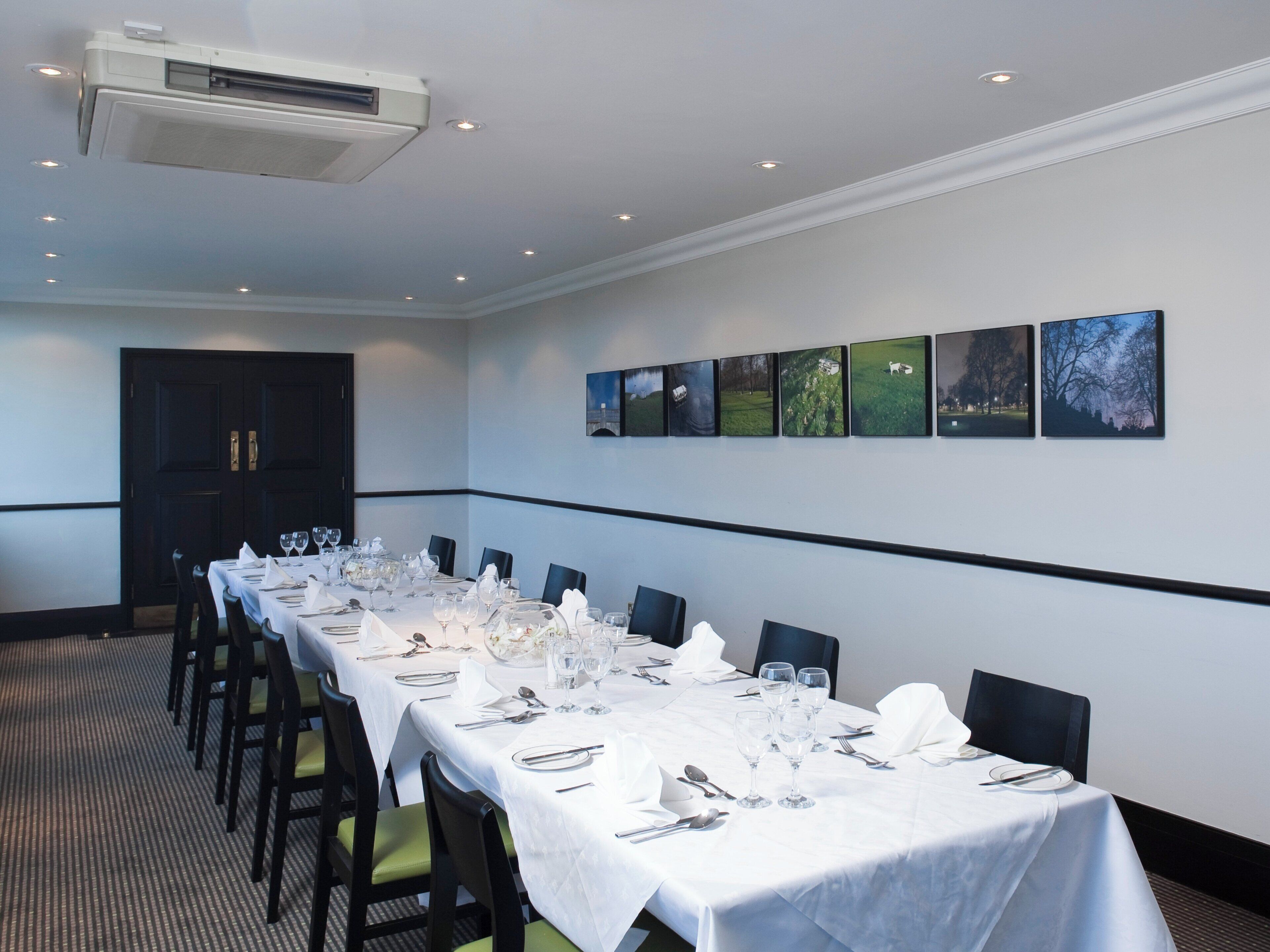 Un salón de conferencias con una larga mesa dispuesta para una reunión, equipado con sillas, mesas y un equipo de aire acondicionado instalado en el techo.