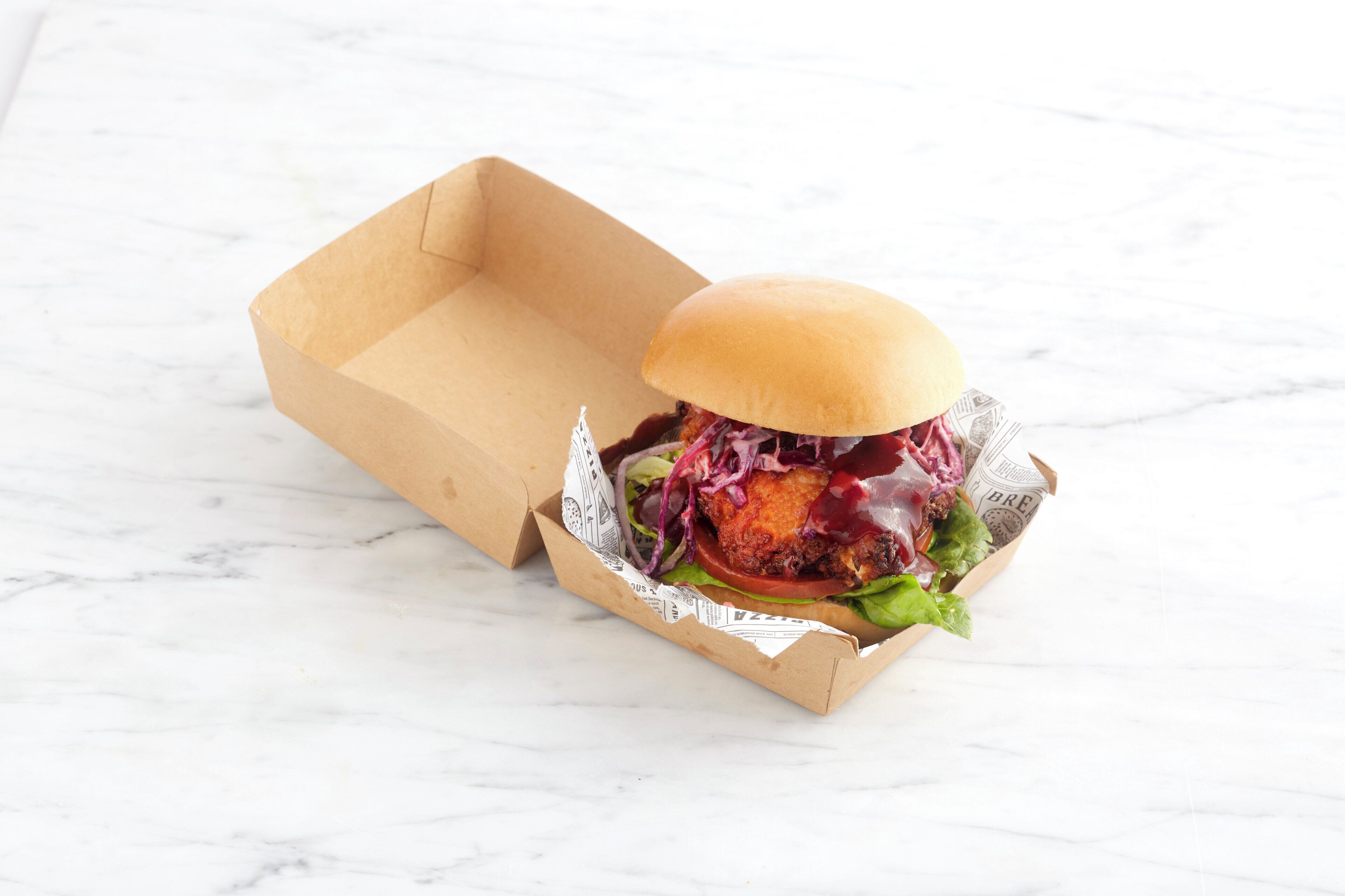 A burger in a paper container on a marble surface.