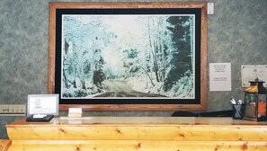 A reception desk with a framed photograph of a snowy forest road, a pet-friendly sign, and a notice about payment methods. - Magnuson Hotel Ely (Ely)