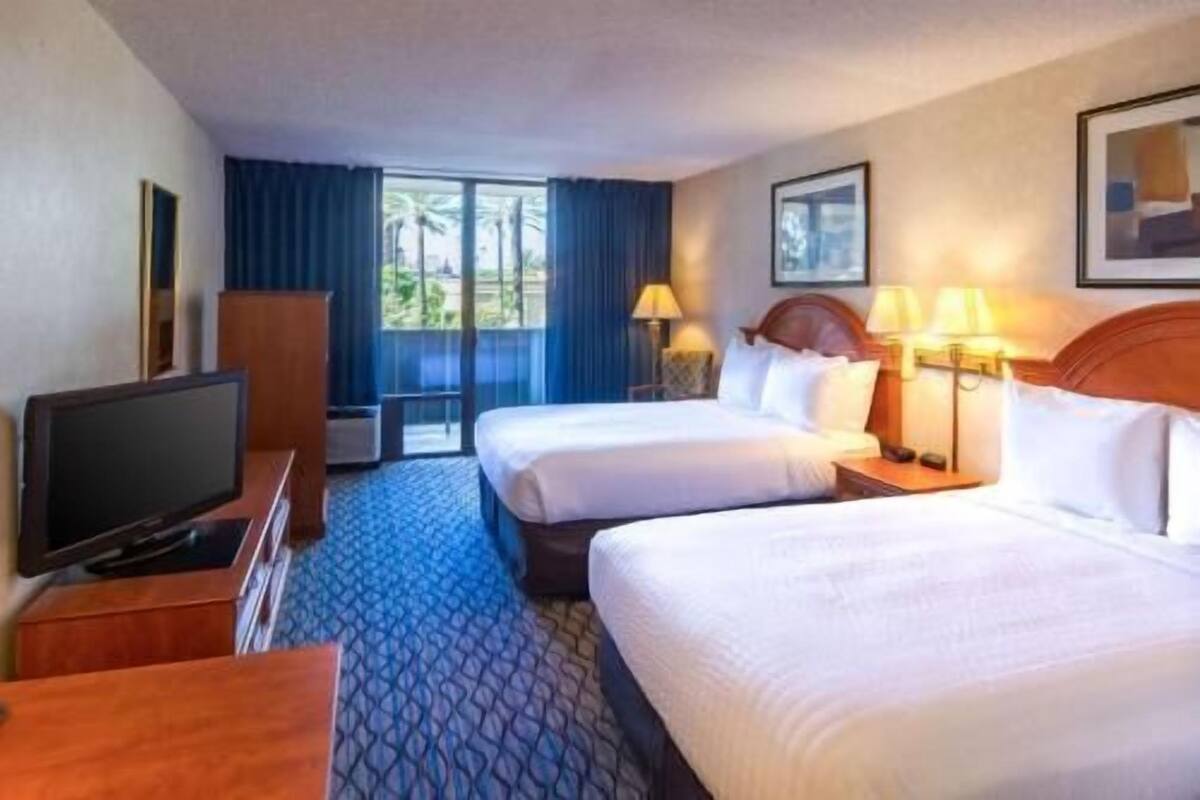 A hotel room with two beds, a TV, a desk, and a window with curtains.
