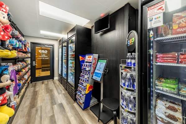 Un pasillo con estantes llenos de refrigerios, una máquina expendedora de Red Bull y un refrigerador de Coca-Cola.