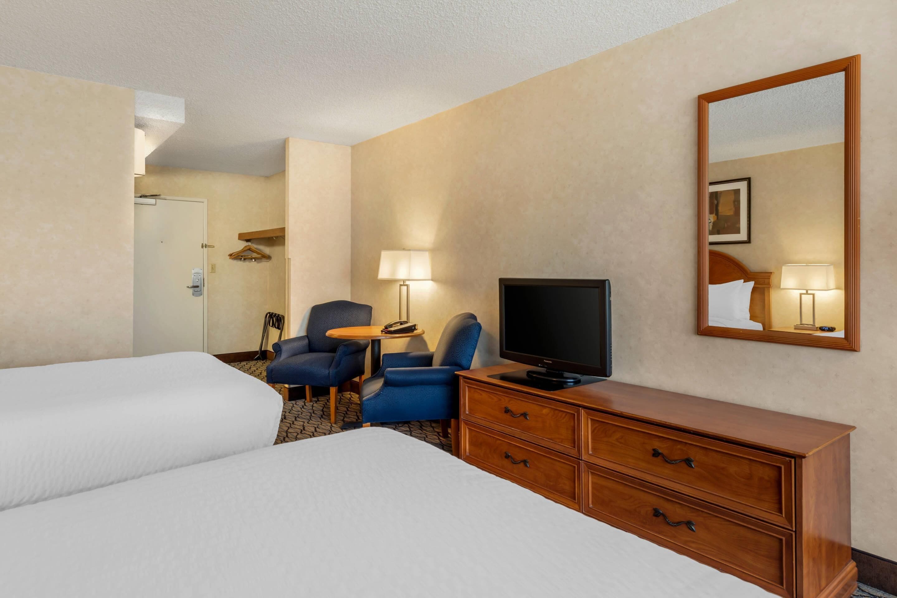 A hotel room with two beds, a TV, a dresser, and two chairs.