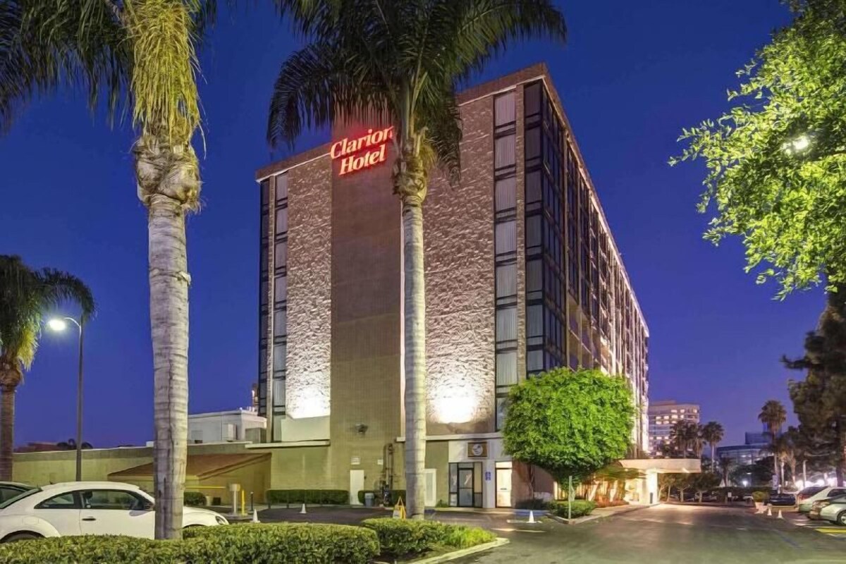 Un hotel con fachada de piedra, un letrero llamativo y un estacionamiento.