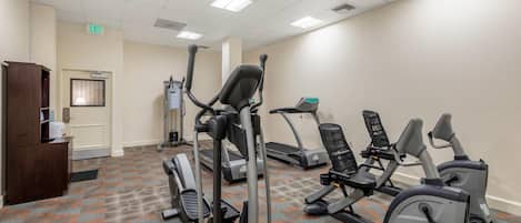 Une salle de sport équipée de tapis de course, de vélos elliptiques et d’un banc de musculation. On y trouve un comptoir d’accueil et un panneau indiquant la sortie sur le mur.