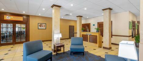 A lobby with two blue armchairs, a reception desk, and a sign for a casual bakery.