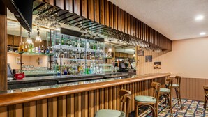 A bar area with wooden paneling, a glass display case with bottles, and bar stools.