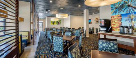 A hotel dining area with patterned floor tiles, wooden slatted partitions, and blue patterned chairs.