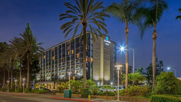 A modern hotel with a glass facade, surrounded by palm trees and well-lit by street lamps.