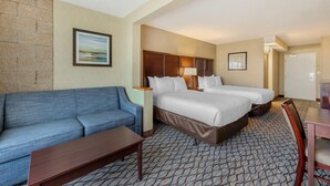 A hotel room with a blue sofa, two beds, a wooden nightstand, a lamp, and a patterned carpet.