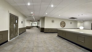 A hotel corridor with a long reception desk, a door at the end, and a wall with decorative elements. - Comancheria Hotel & Convention Center (Lawton)