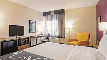 Ein Hotelzimmer mit Bett, Schreibtisch mit Fernseher, Stuhl und einem Fenster mit Vorhängen.