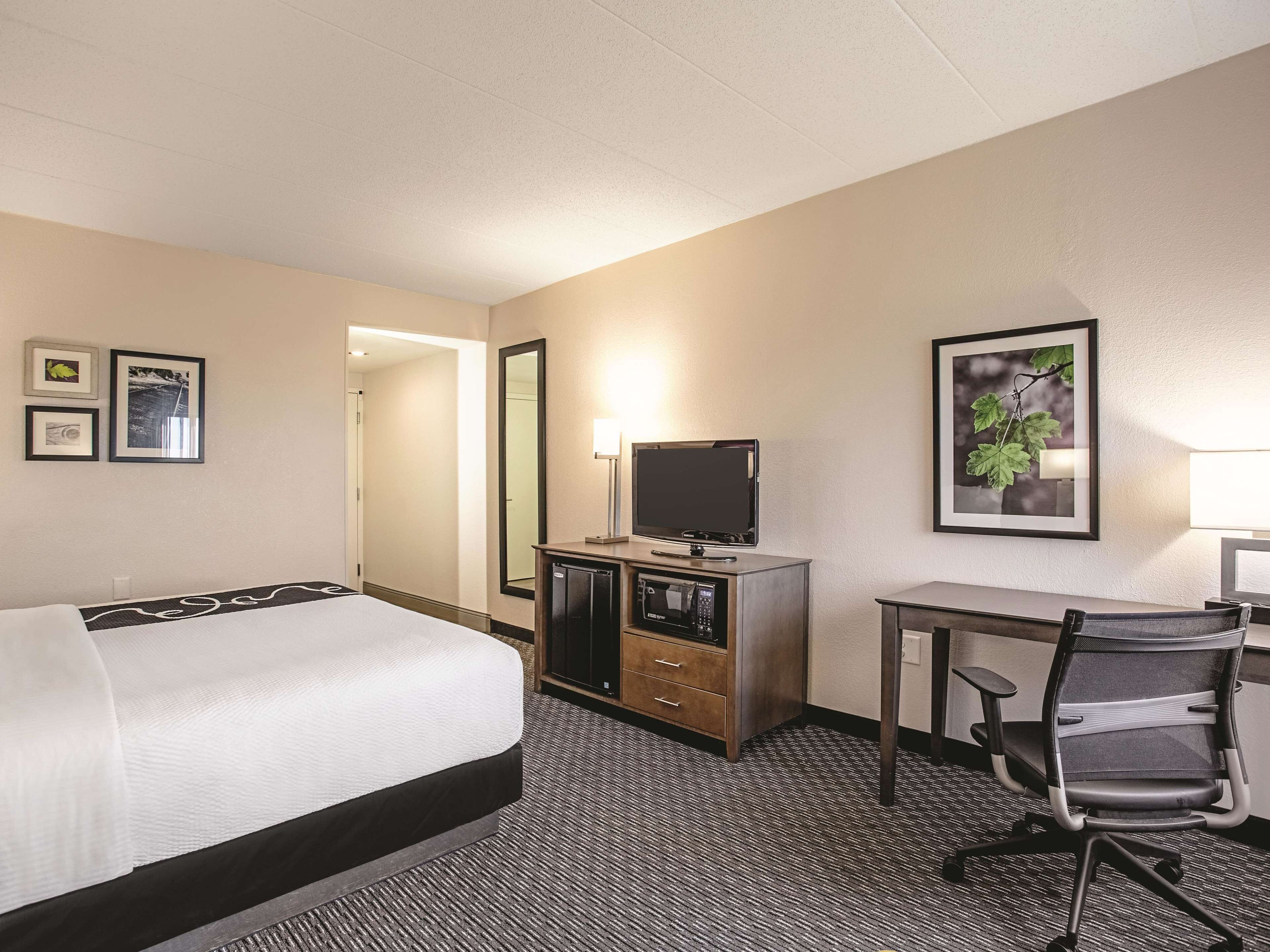 A hotel room with a bed, a desk with a computer, a chair, a TV, and a microwave.