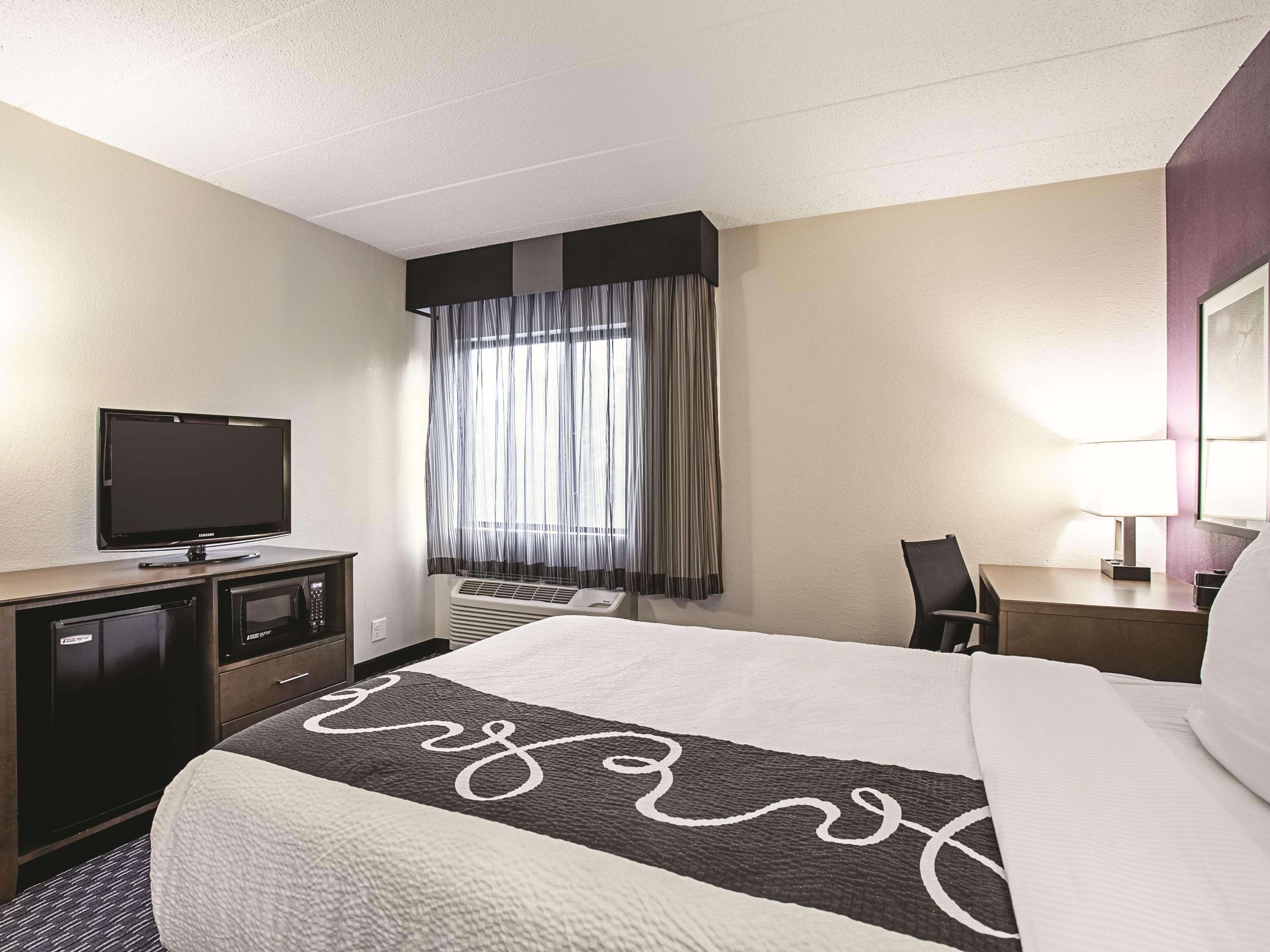 Una habitación de hotel con una cama, un escritorio, un televisor y una ventana con cortinas.