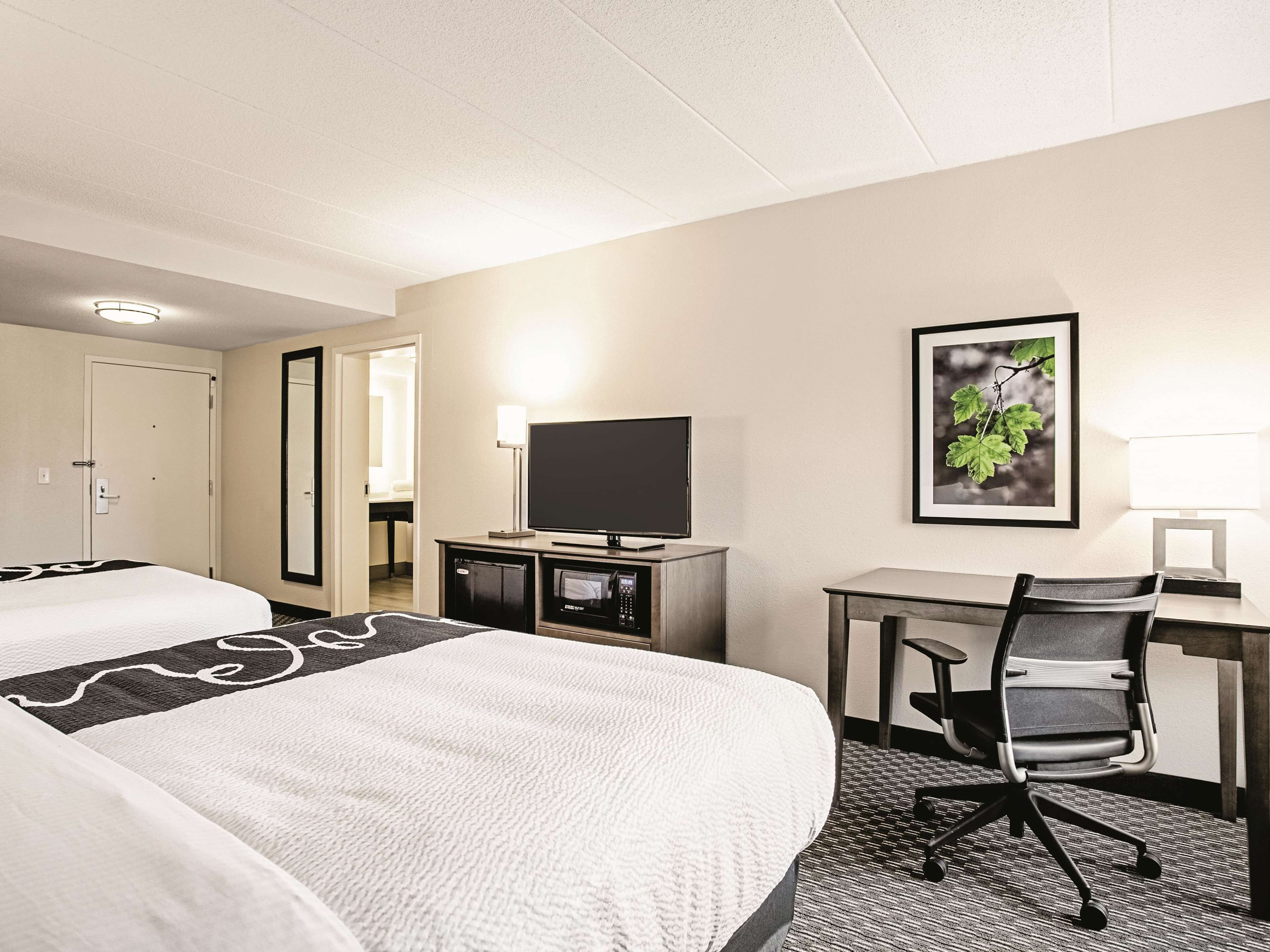 A hotel room with two beds, a desk, a chair, a television, and a framed picture on the wall.