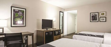 A hotel room with a desk, a television, a bed with a quilt, and a mirror.