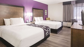 A hotel room with two beds, a desk, a TV, a lamp, and a window with curtains.