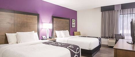 A hotel room with two beds, a desk, a TV, a lamp, and a window with curtains.