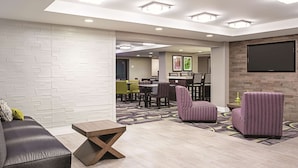 A modern hotel lobby with a seating area, a reception desk, and a dining area.