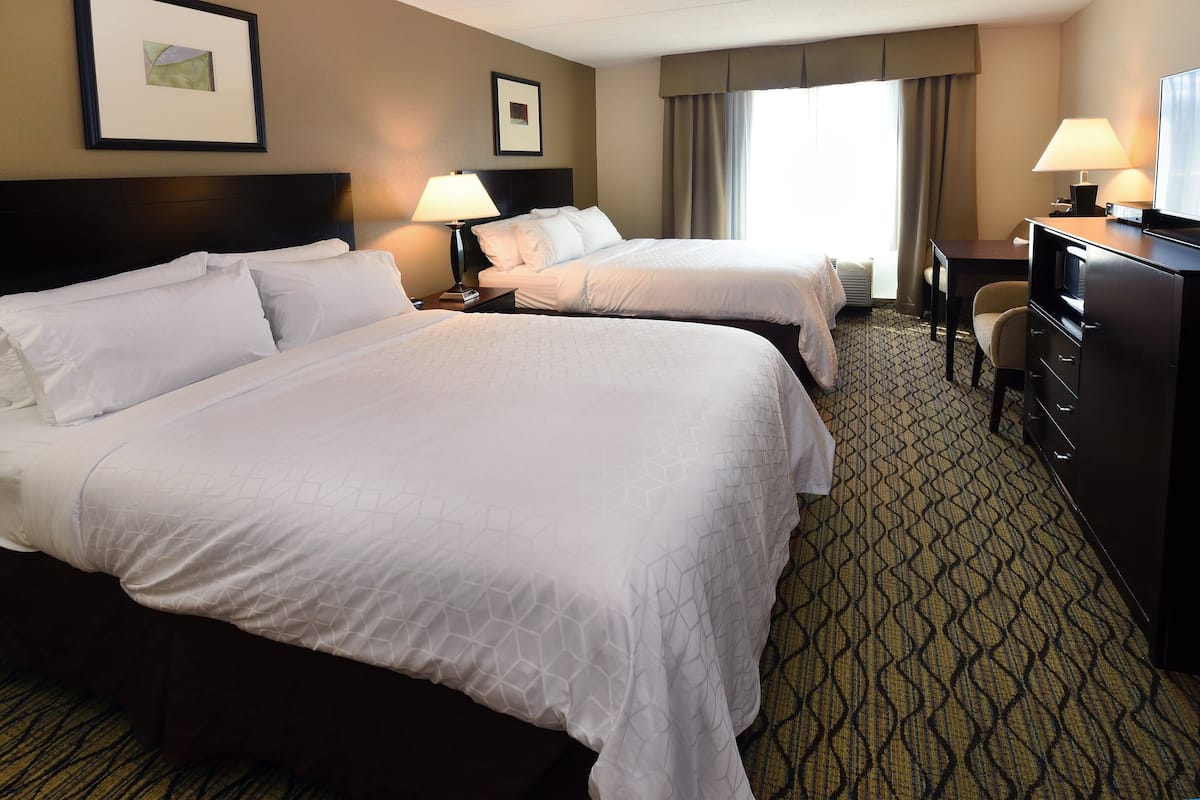 A hotel room with two beds, a desk, a chair, and a TV.